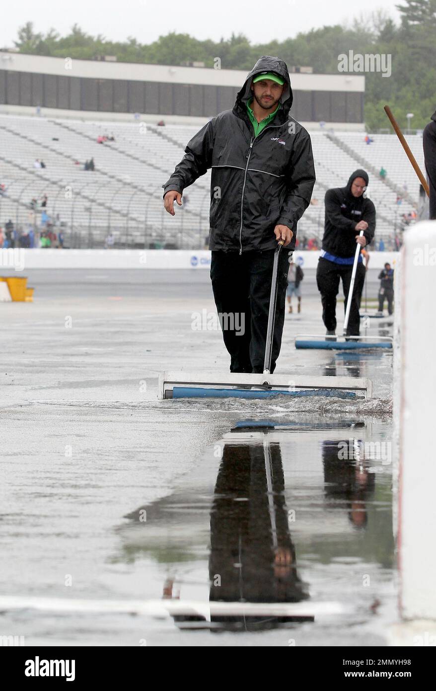 Crew members use rollers to remove water from pit lane during a weather