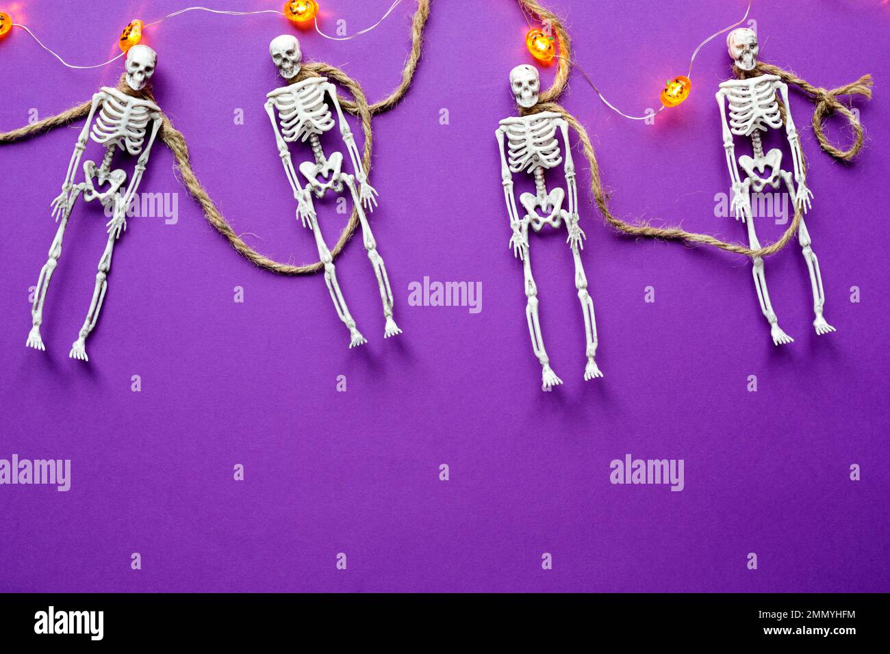 Halloween layout of garland of skeletons on a rope, glowing Jack o Lantern, pumpkins on a purple background. Flat lay horror and a terrible holiday Stock Photo