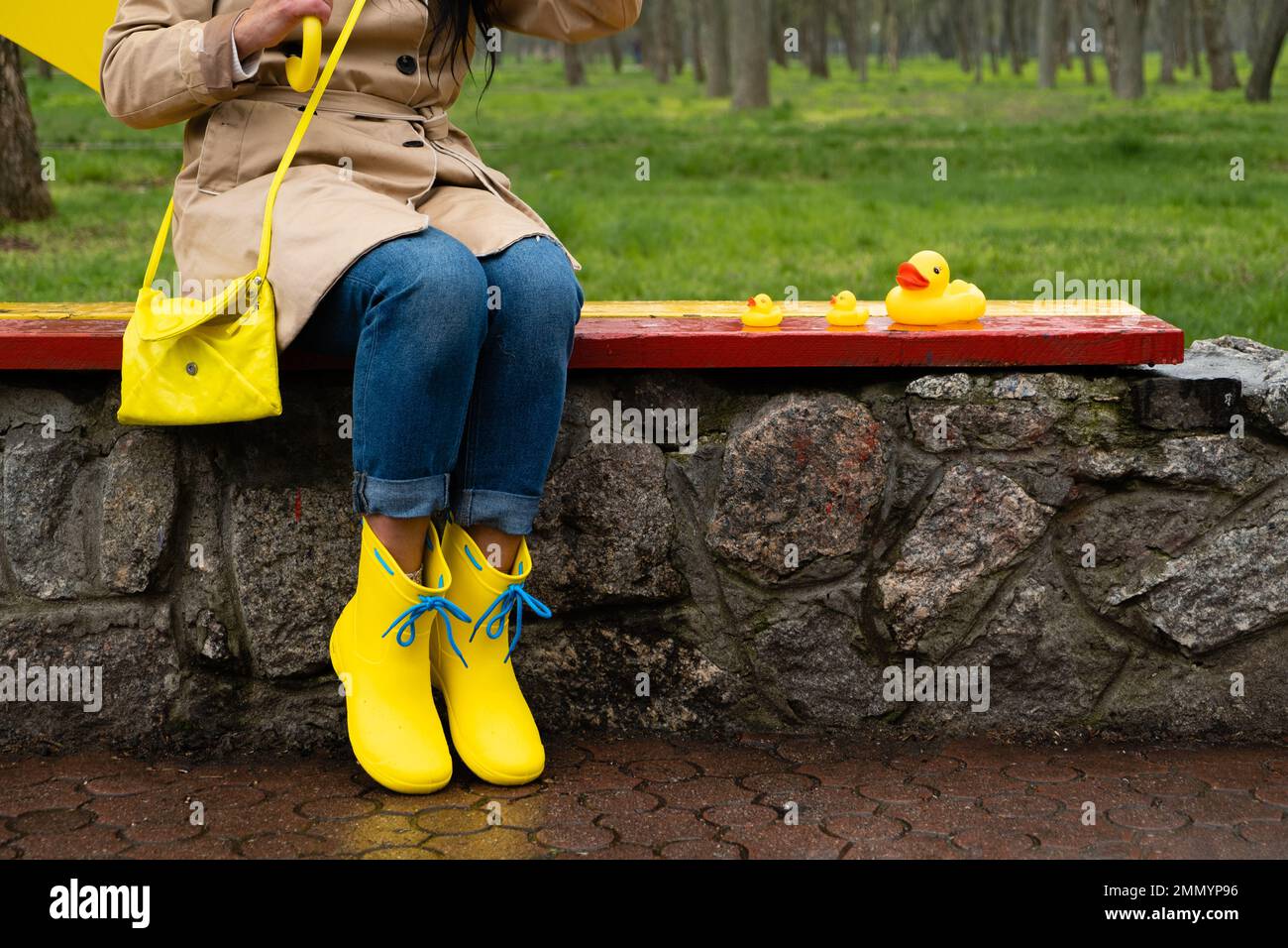 Stress resilience and mental health, no depression concept. Womens legs in yellow rubber boots and a yellow rubber duck in the rain in the park. Stock Photo