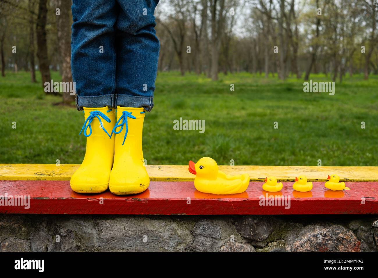 Stress resilience and mental health, no depression concept. Womens legs in yellow rubber boots and a yellow rubber duck in the rain in the park. Stock Photo