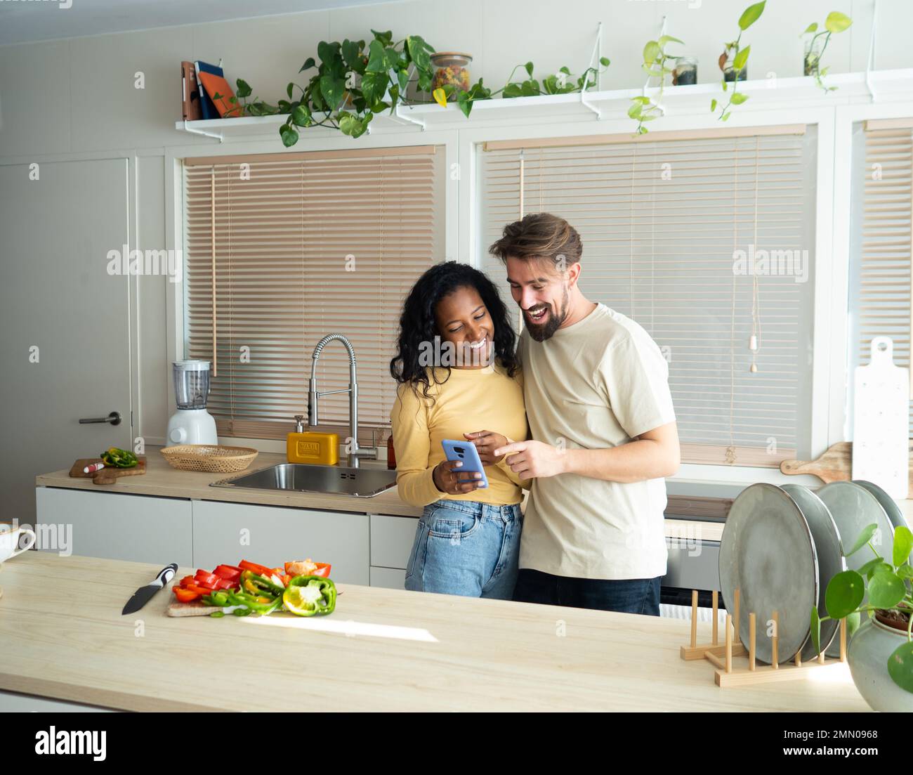 Young heterosexual diverse couple looking at mobile in a kitchen Stock Photo