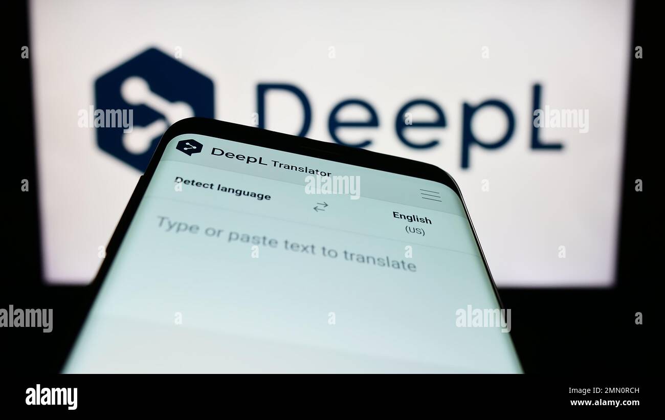 Mobile phone with webpage of neural machine translator DeepL on screen in front of logo. Focus on top-left of phone display. Stock Photo