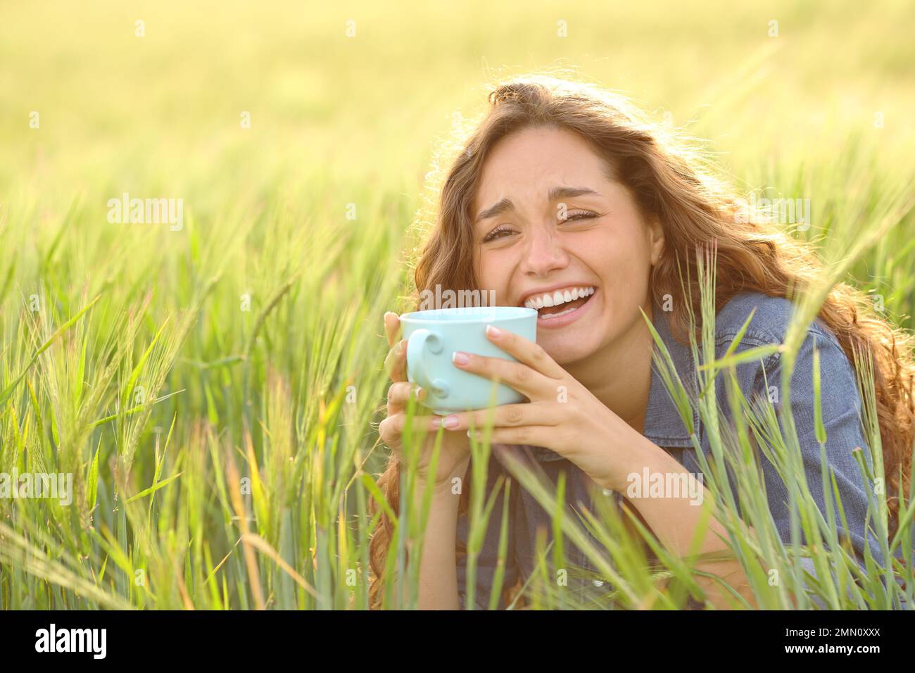 Happy woman laughing drinking coffee in a field and looking at camera Stock Photo