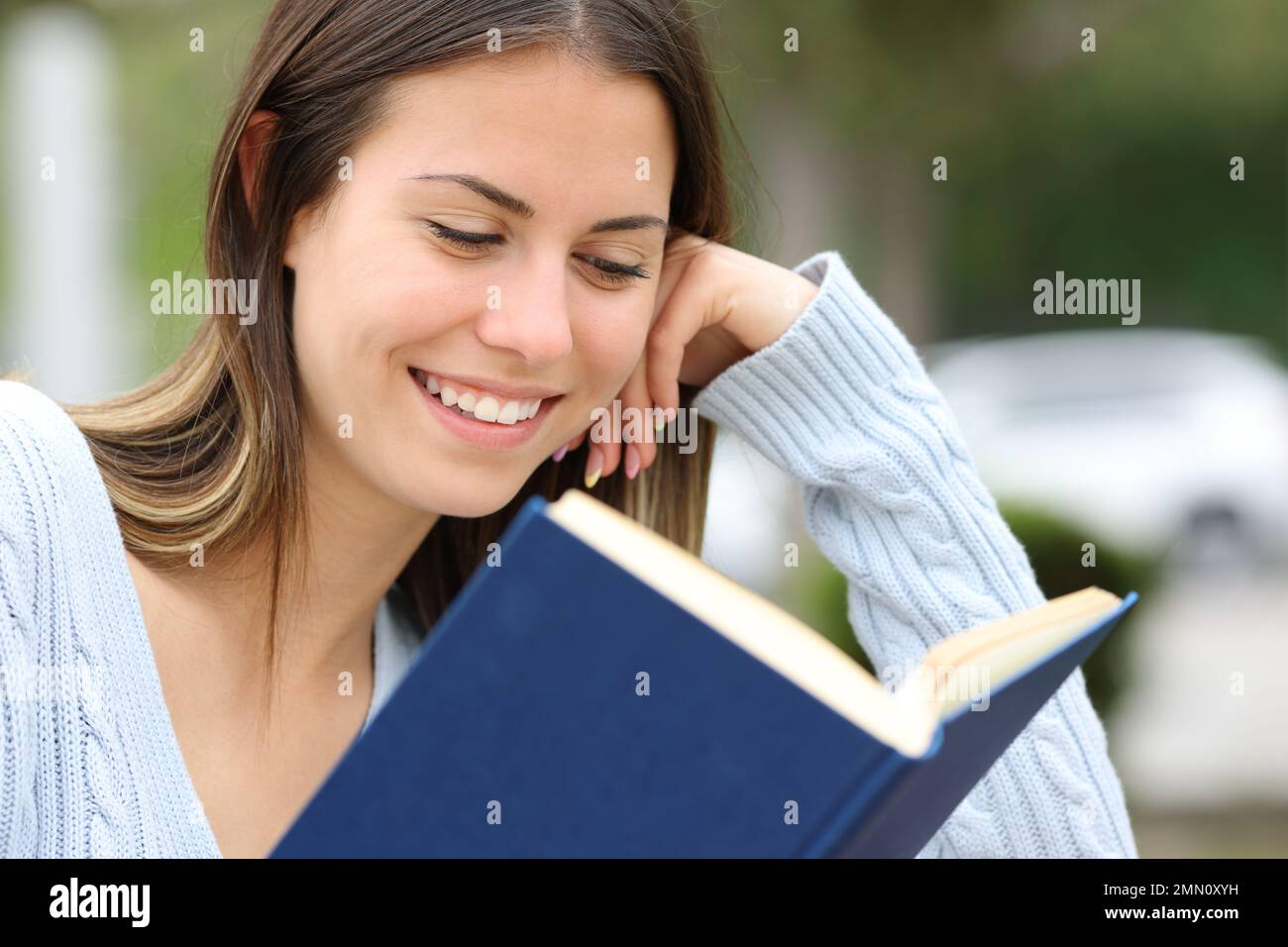 Happy teen reading a book outside in a park Stock Photo