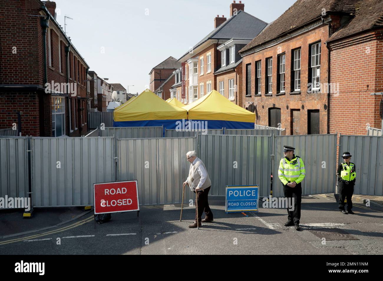 FILE - In this Friday, July 6, 2018 file photo, an elderly man walks by as British police officers guard metal fencing surrounding tents set up by search teams at the end of Rollestone Street, outside the location of the John Baker House for homeless people in Salisbury, England. British detectives investigating the poisoning of two people by the nerve agent Novichok in southern England said Friday, July 13, 2018 that scientists have found the source of the deadly substance. (AP Photo/Matt Dunham, File) Stock Photo