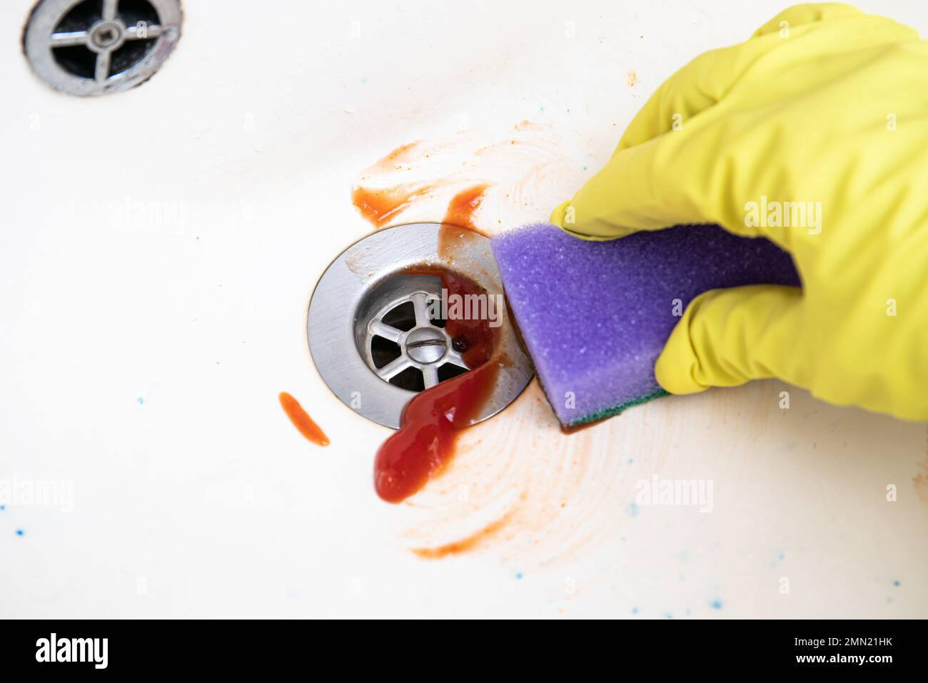 Close up view of woman hand cleaning sink with tomato ketchup, scrubbing with cleaning sponge. Alternative lifestyle concept. Stock Photo
