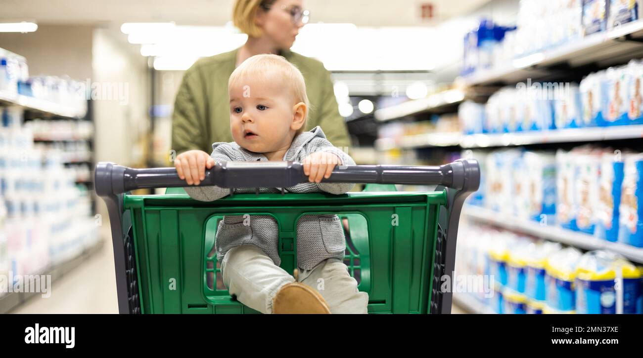 Mother pushing shopping cart with her infant baby boy child down