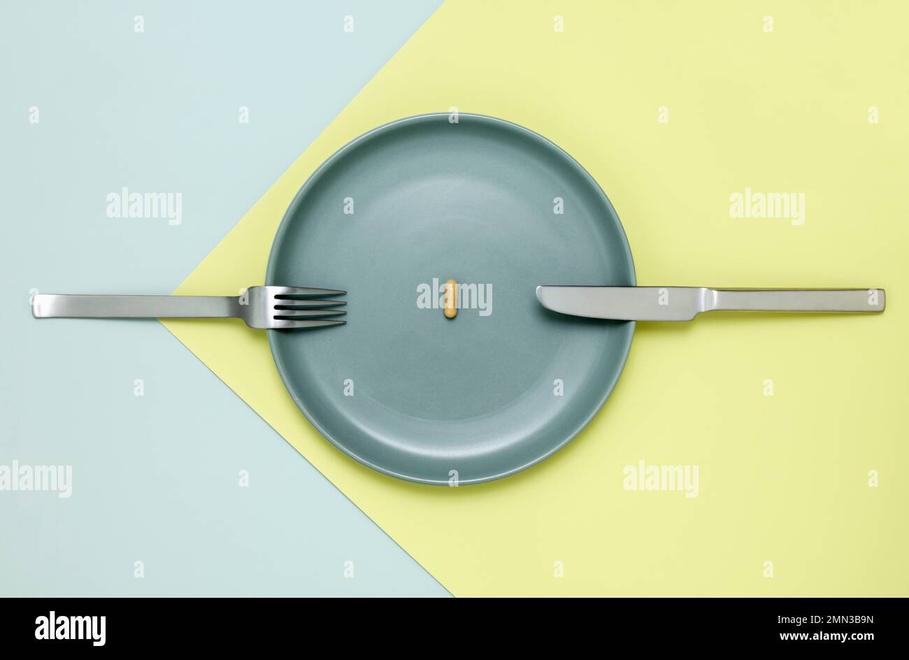 One vitamin tablet on blue green plate with knife and folk from above Stock Photo