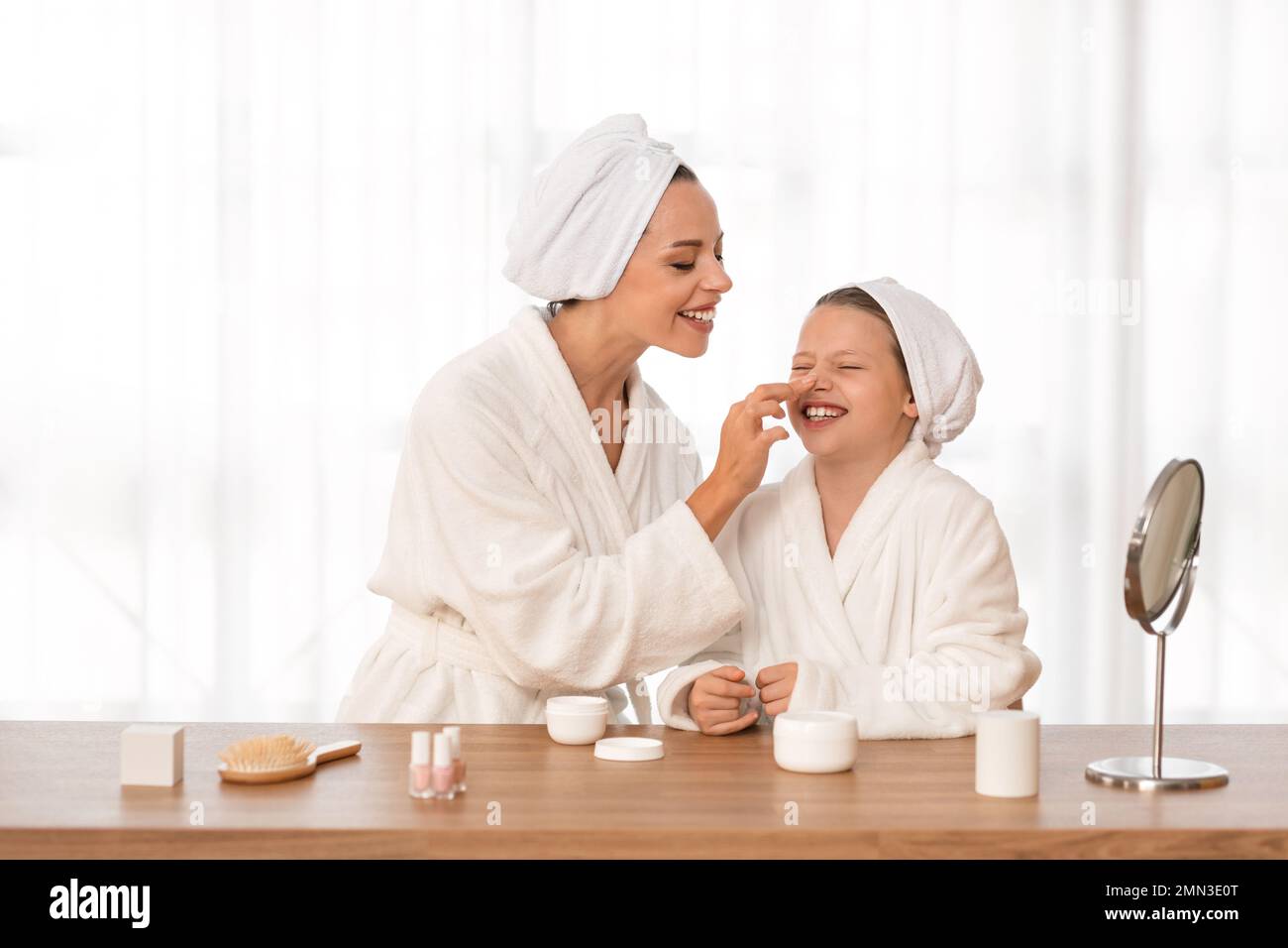 Happy mother and little daughter in bathrobes and towels applying face cream Stock Photo