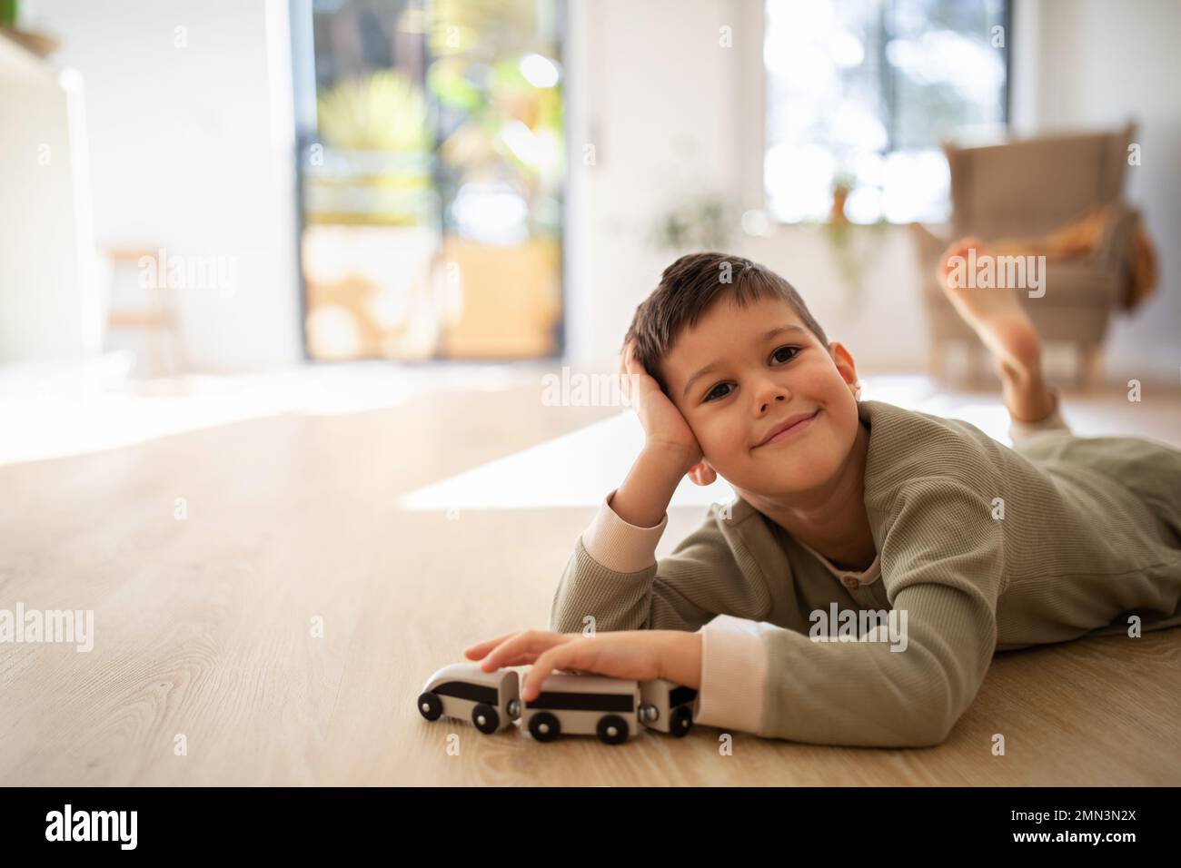 Cheerful pensive small european boy in pajamas lies on floor, plays with cars alone, enjoy rest and spare time Stock Photo