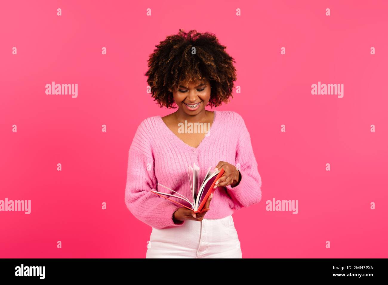 Smiling smart young african american curly lady student in casual reading book, diary Stock Photo