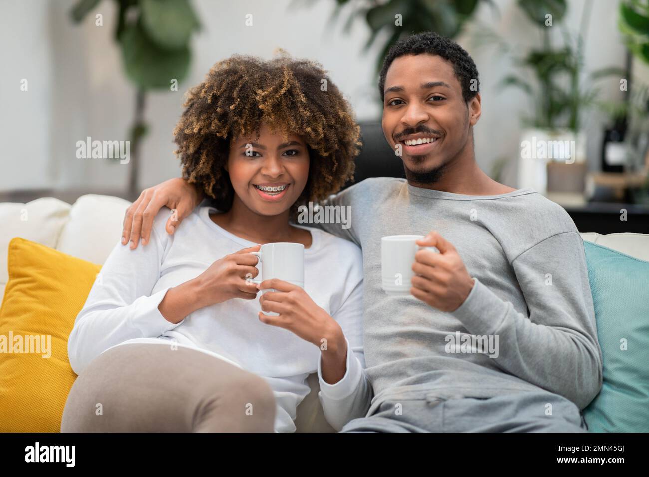 Cute African Couple Posing On Couch At Home Drinking Coffee Stock cute-african-couple-posing-on-couch-at-home-drinking-coffee-stock