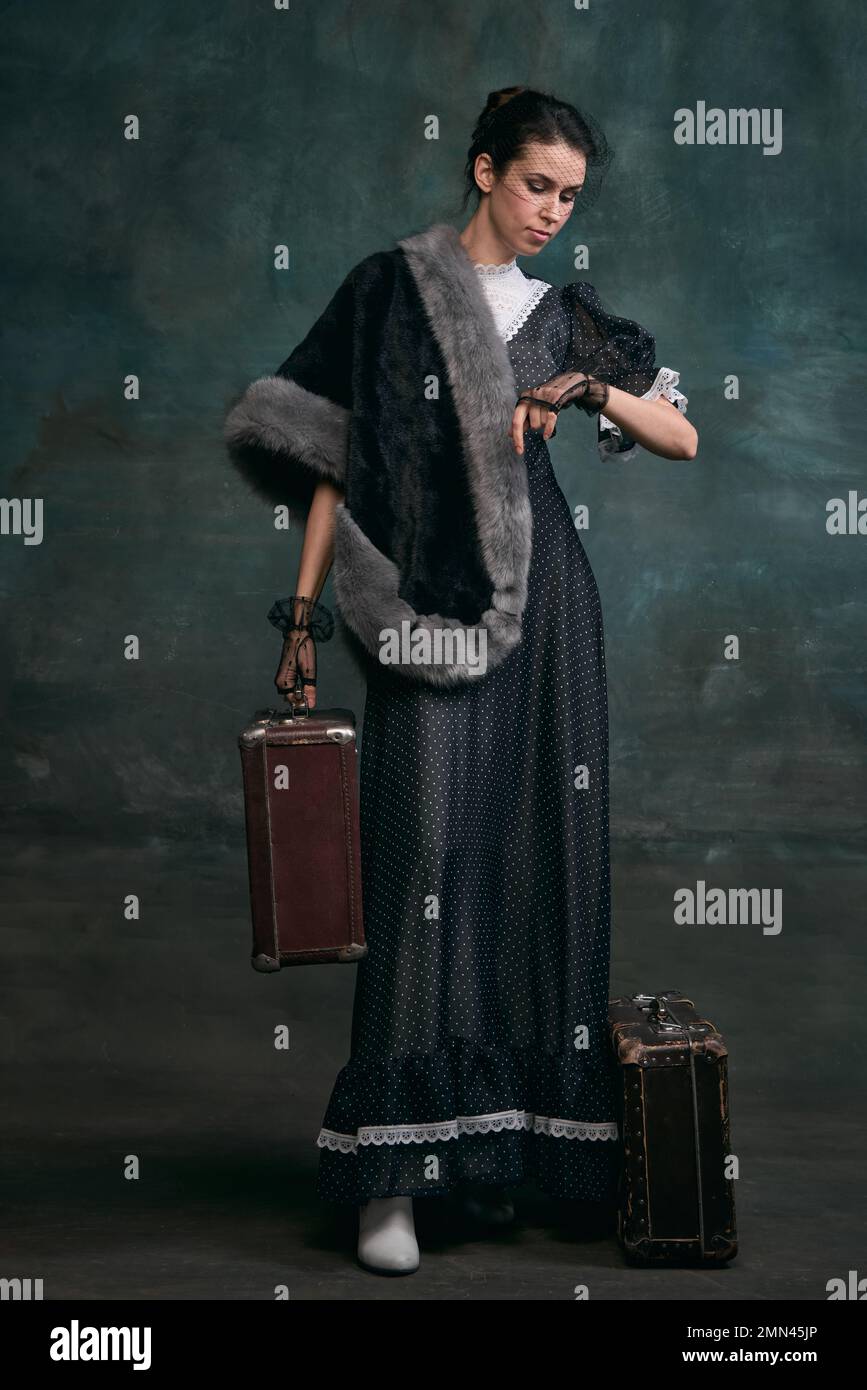 Travelling. Time. Beautiful woman in image of Anna Karenina with retro suitcases over vintage dark green background. Concept of literature character Stock Photo