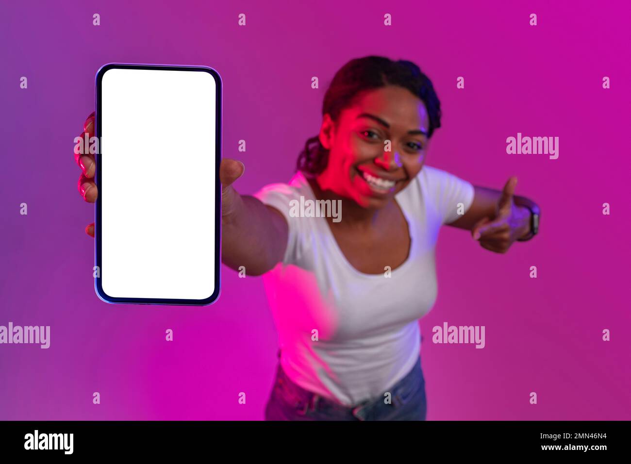 Cheerful black woman showing smartphone with empty white screen in neon light Stock Photo