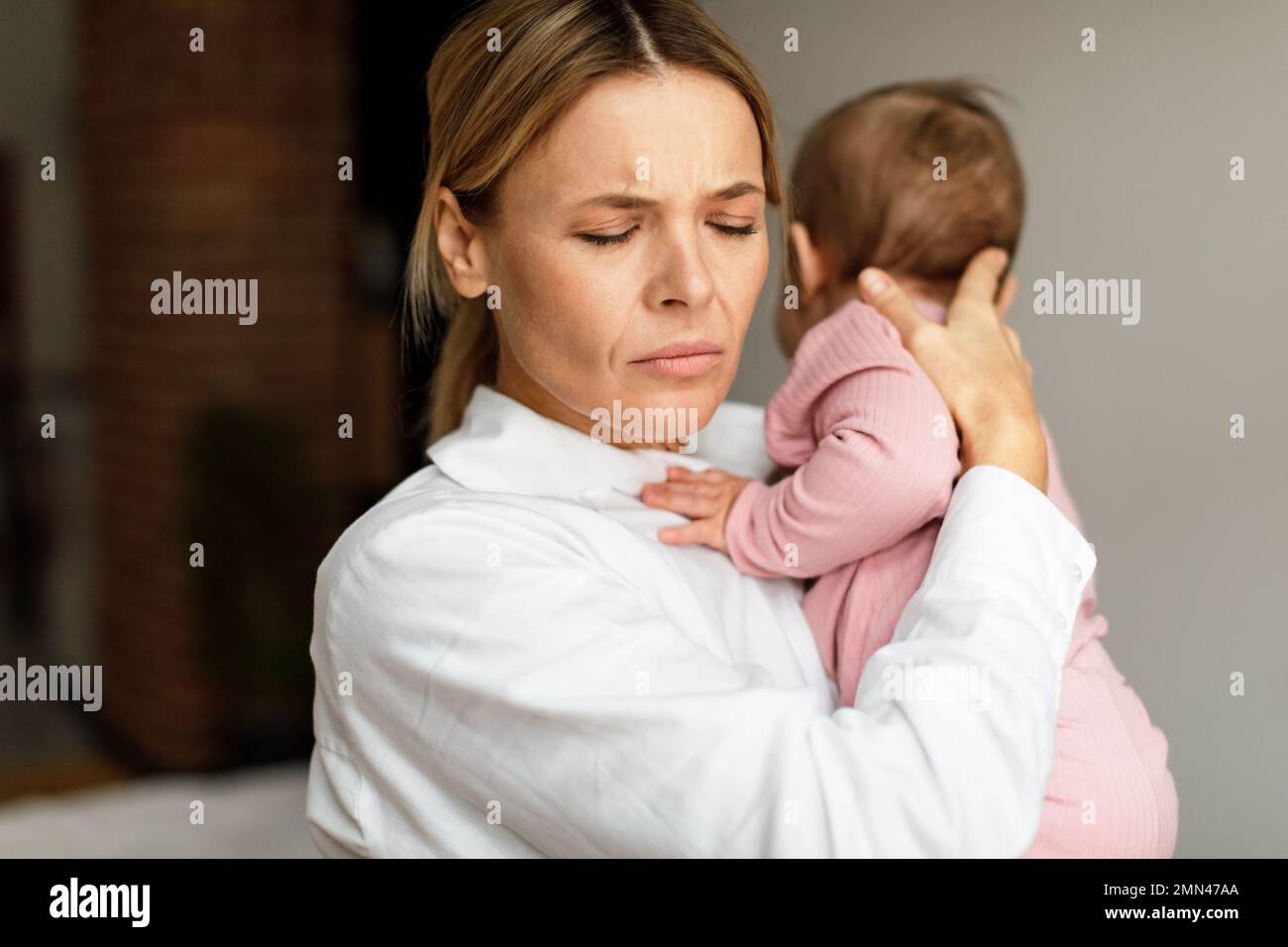 Exhausted mother holding little baby, standing at home interior in