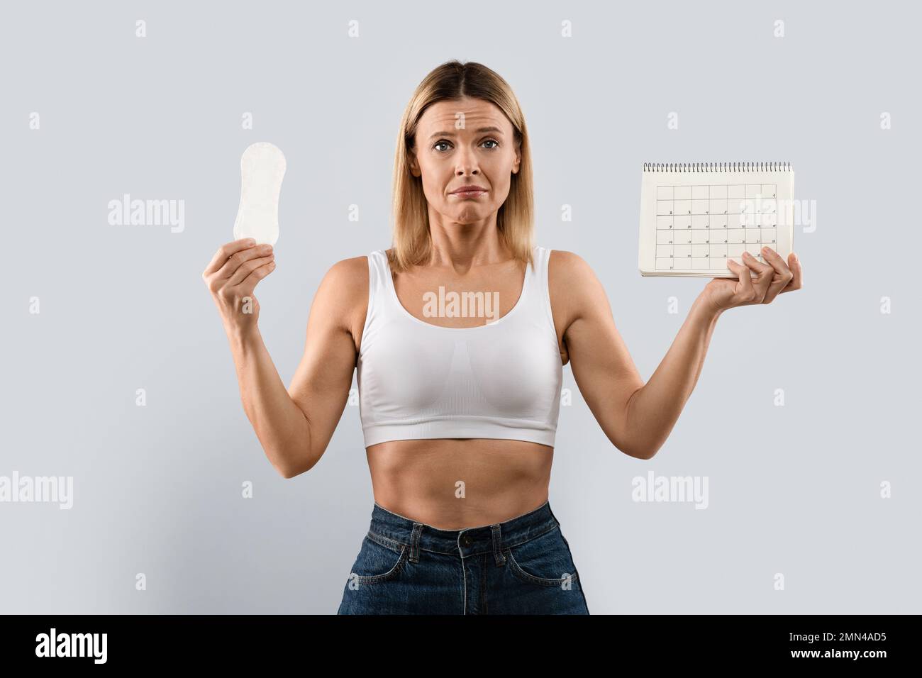 Unhappy middle aged woman demonstrates periods calendar and sanitary napkin Stock Photo