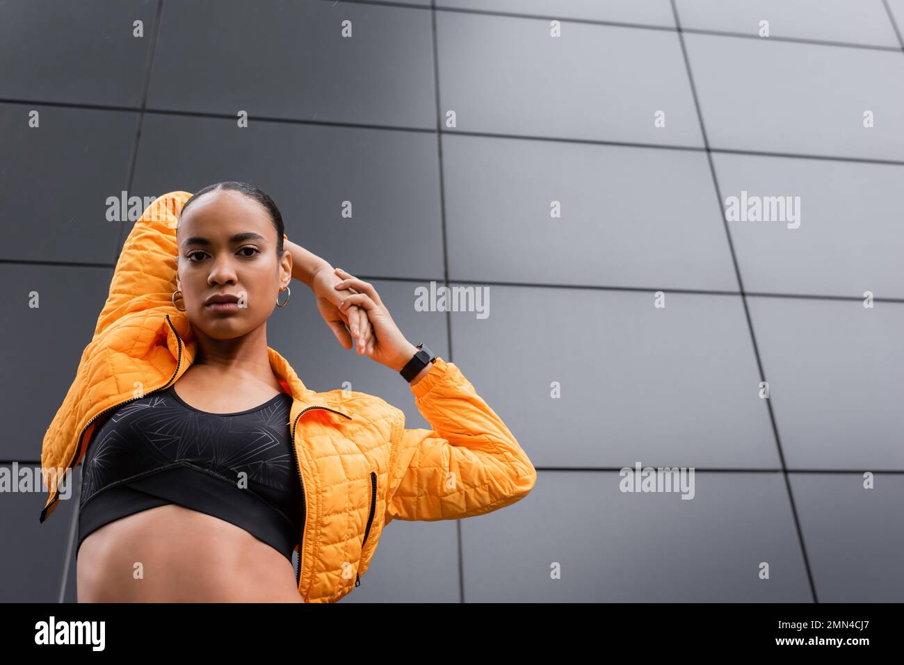 low angle view of african american sportswoman in sports bra and puffer  jacket warming up near grey building Stock Photo - Alamy