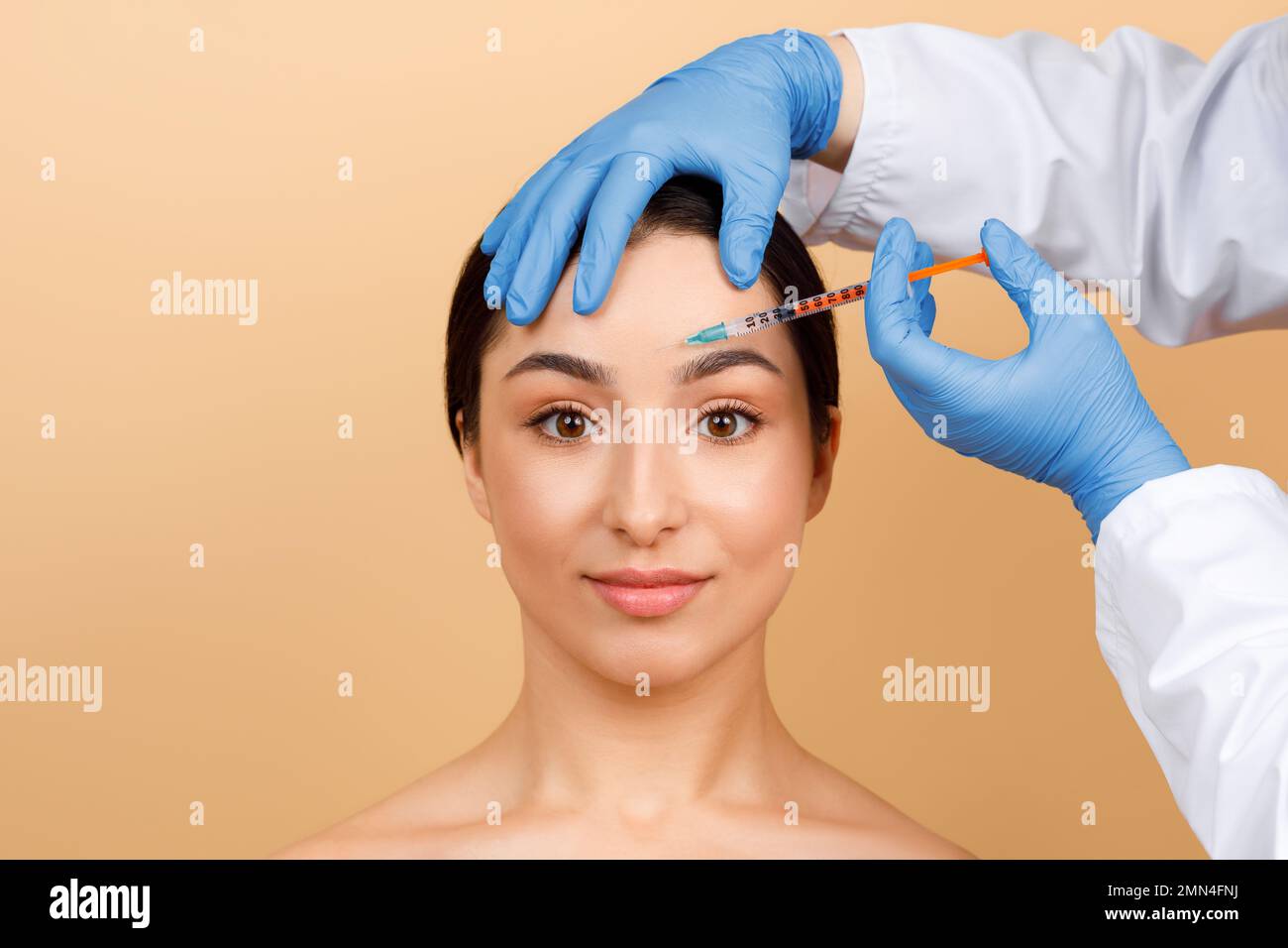 Cosmetologist Doctor Making Botox Injection In Interbrow Zone To Young Indian Woman Stock Photo