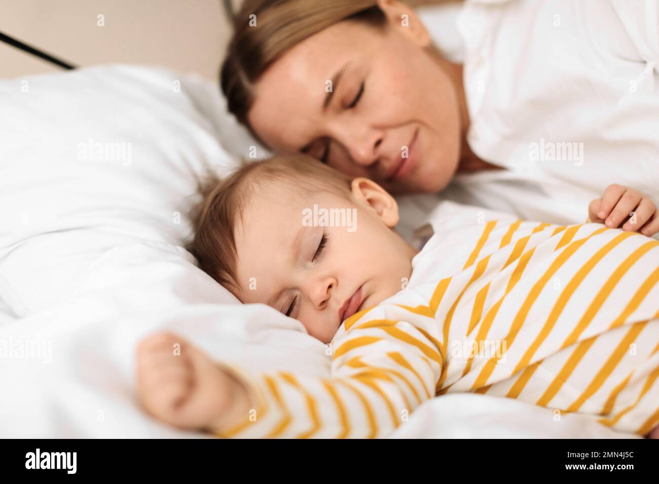 Bed-sharing with baby concept. Adorable infant child girl sleeping with her mother on bed in bedroom during daytime Stock Photo