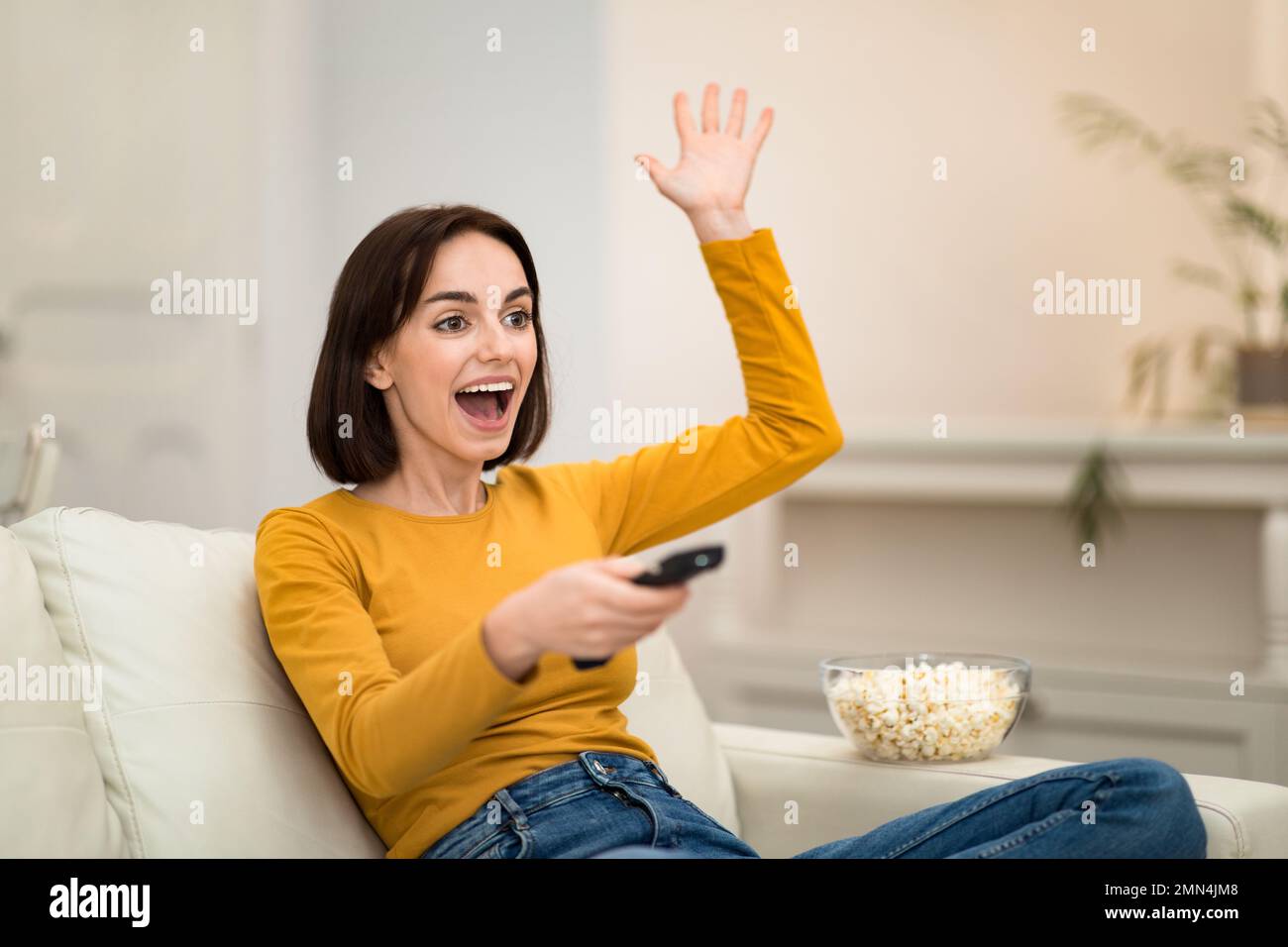 Emotional woman watching TV show with popcorn at home Stock Photo