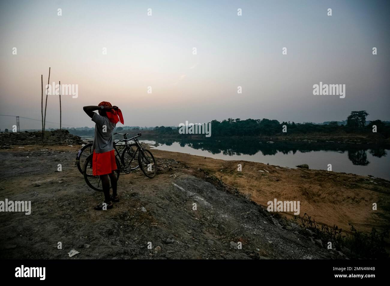 A construction worker, tying headscarf in the cold months of winters in India, with his Cycle by the River Subarnarekha in Jamshedpur. Stock Photo