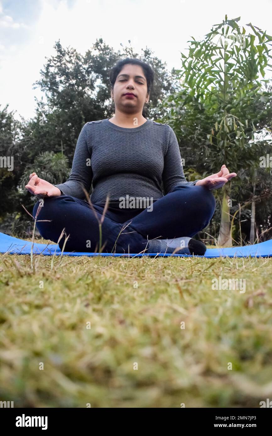 Young Indian woman practicing yoga outdoor in a park. Beautiful girl practice basic yoga pose. Calmness and relax, female happiness. Basic Yoga poses Stock Photo
