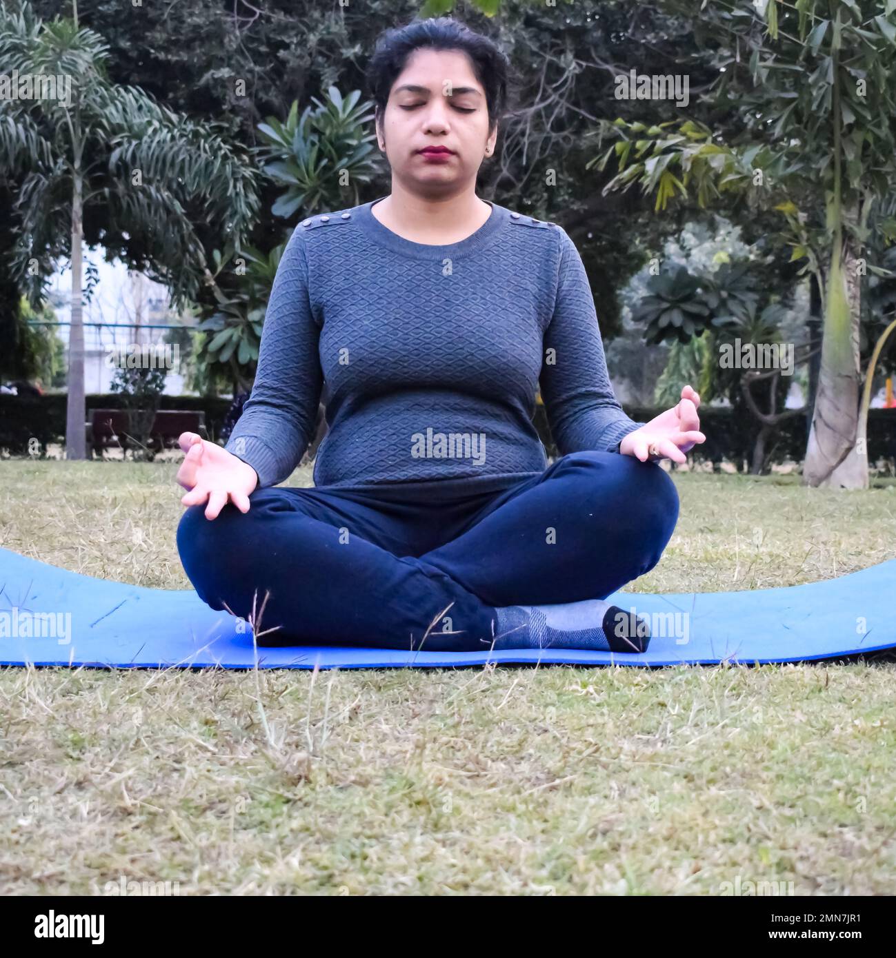 Young Indian woman practicing yoga outdoor in a park. Beautiful girl practice basic yoga pose. Calmness and relax, female happiness. Basic Yoga poses Stock Photo