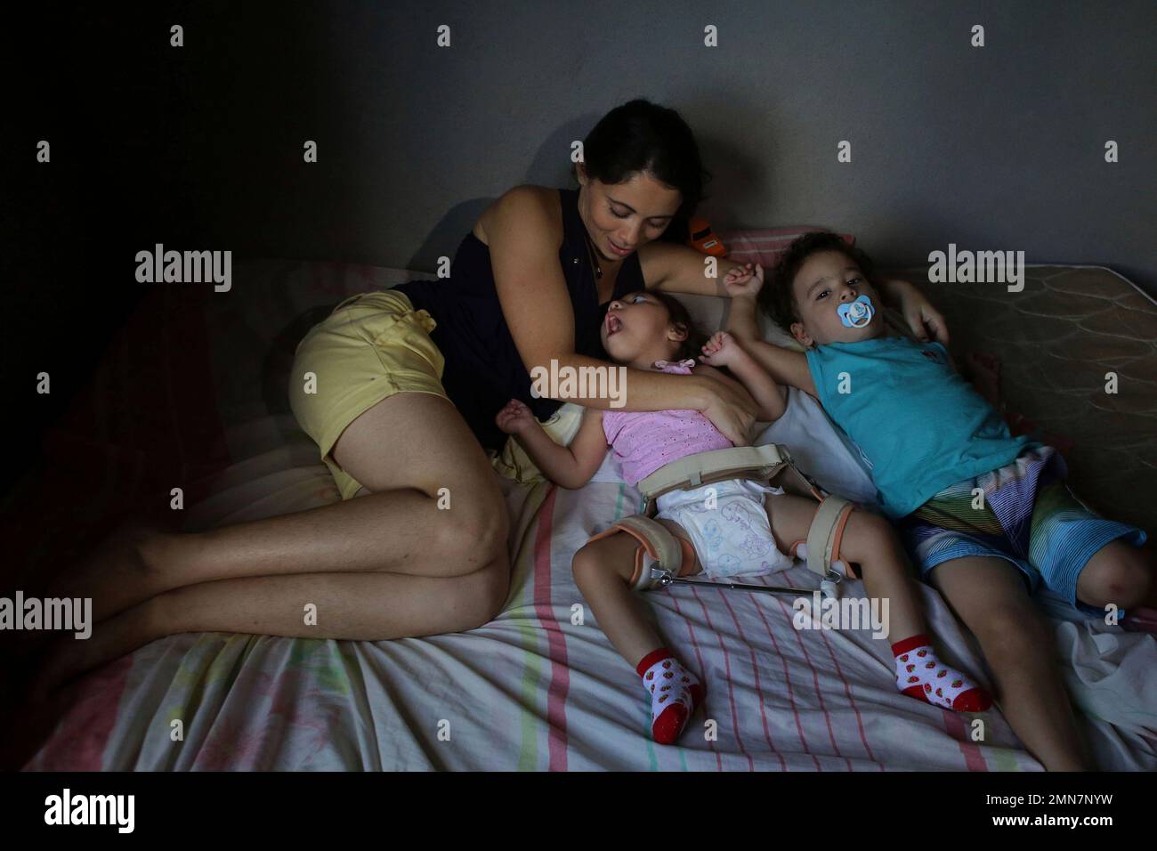In this May 4, 2018 photo, Cassiana Severina da Silva, lies on a bed with  her 2-year-old twins, Melissa Vitoria, who was born with the Zika-caused  microcephaly birth defect, and Edson Junior,