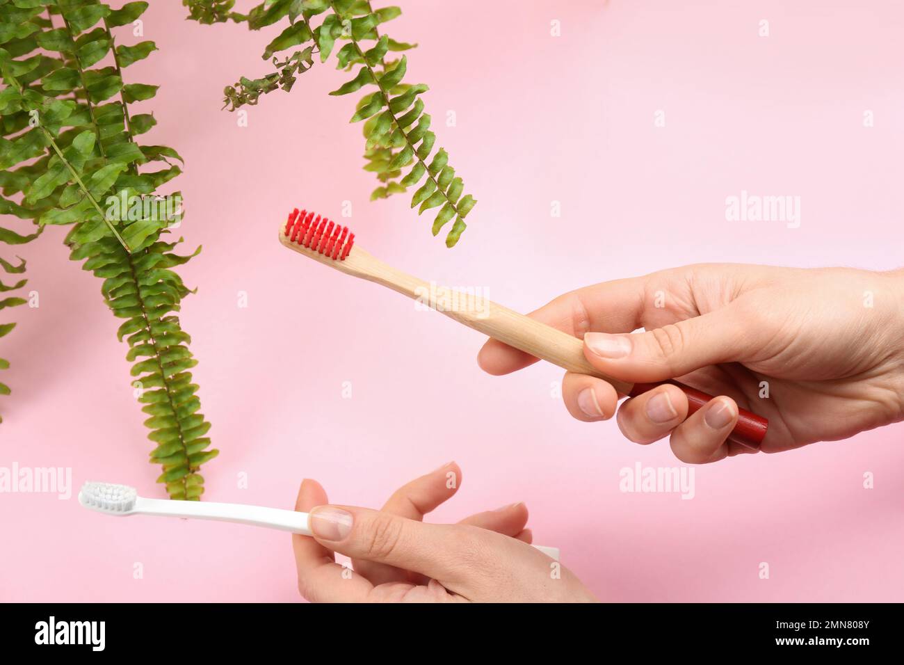 Woman holding natural bamboo and plastic toothbrushes on pink background Stock Photo
