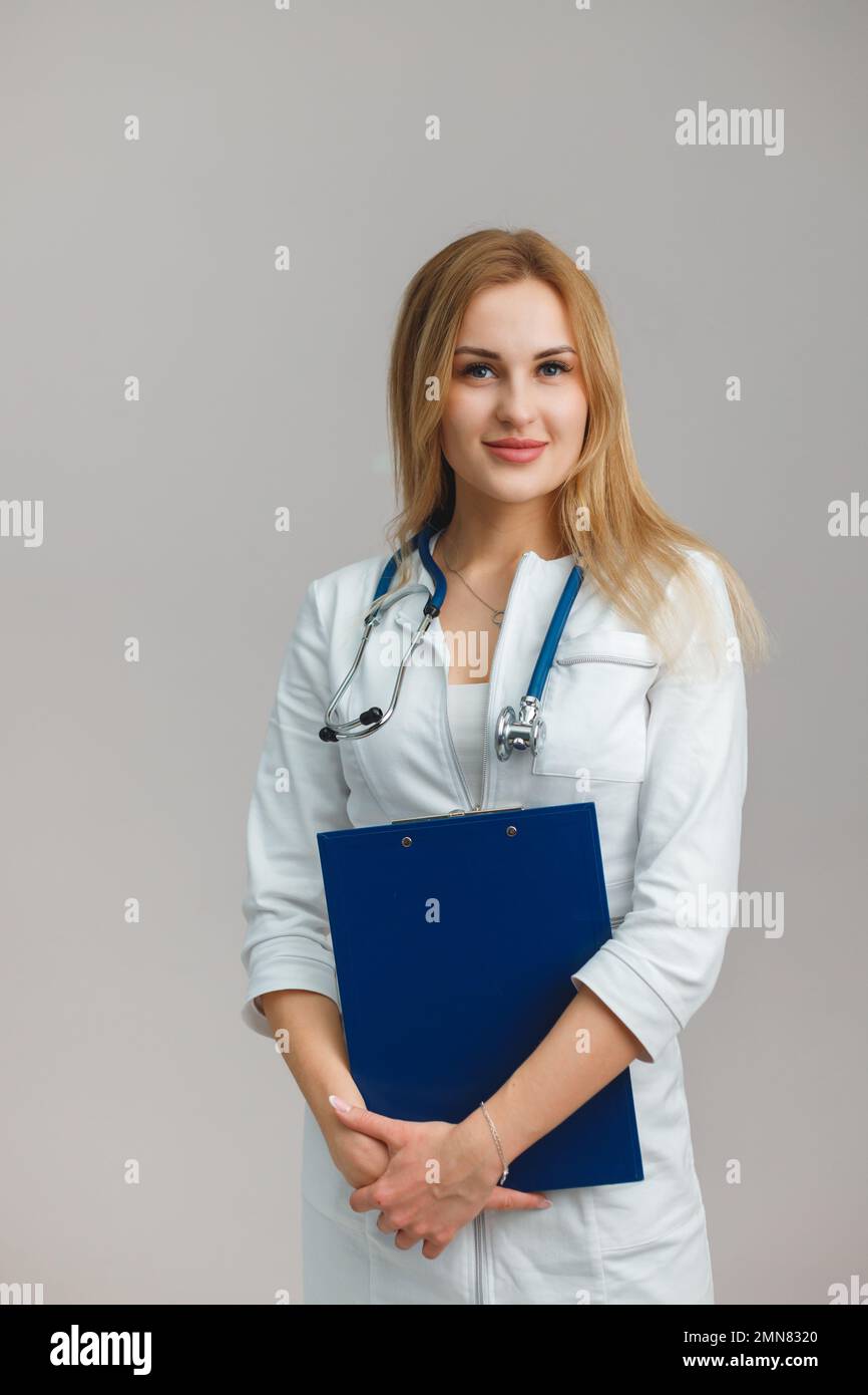 Young European Female Doctor Portrait with stethoscope and folder wearing white robe. Portrait on plain background. Appointment Stock Photo