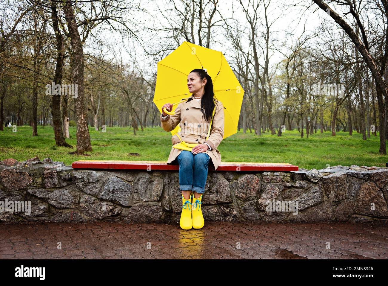 Coping with stress and anxiety. Practicing mindfulness and relaxation techniques. Happy senior woman in yellow rain coat with yellow umbrella walking Stock Photo