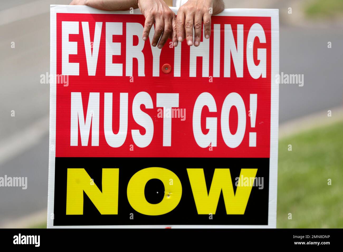 A man holds up a sign announcing the going out of business sale at a