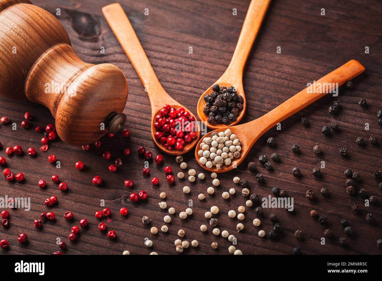 Different types of peppercorns black, white, red and a pepper mill on