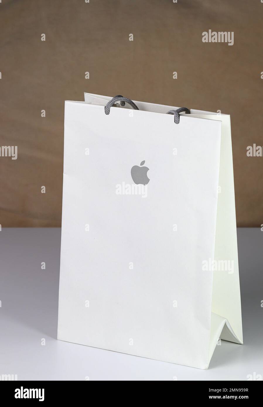 White paper shopping bag, present bag with Apple brand logo standing on white table with shallow focus. Stock Photo