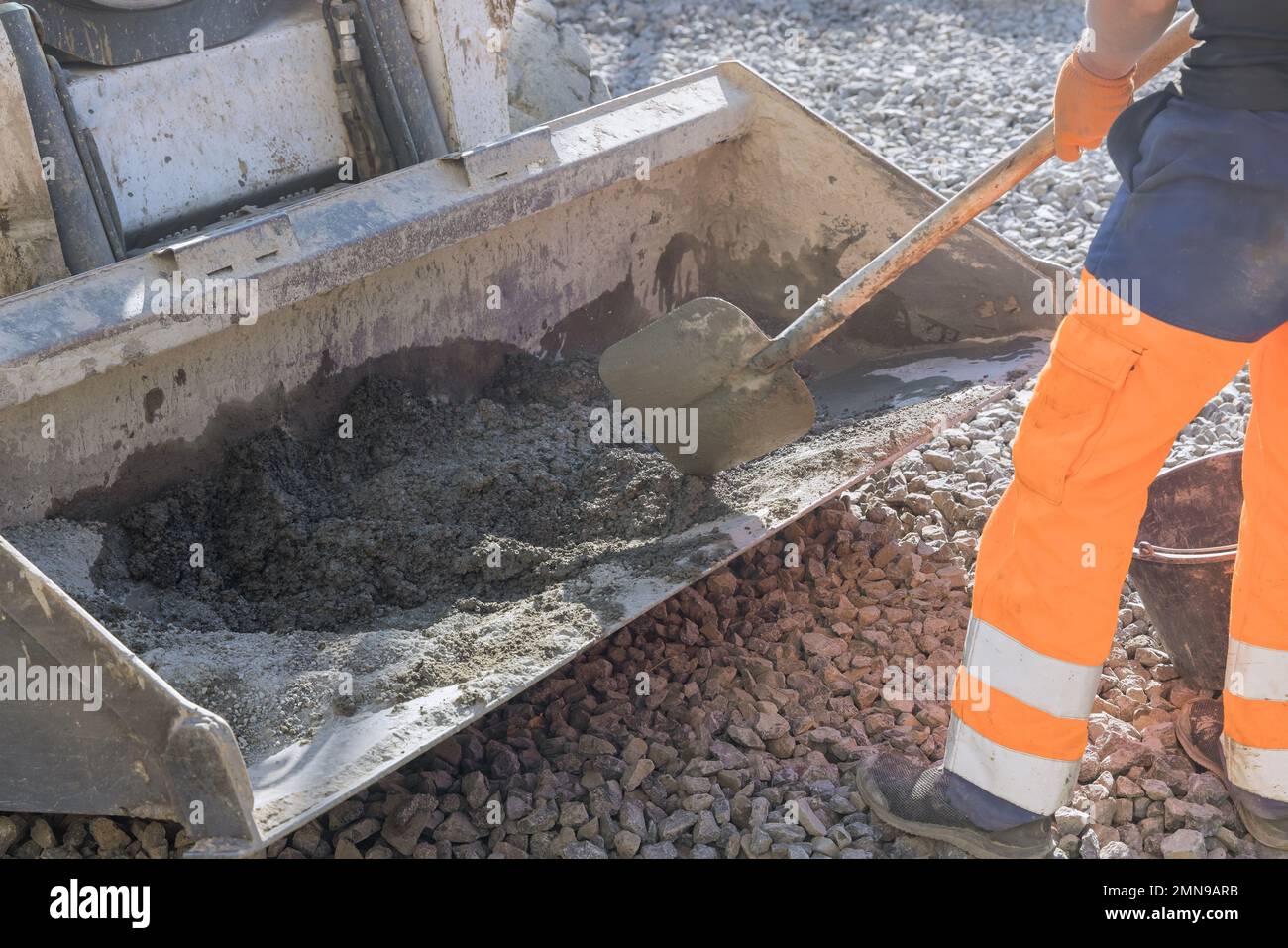An excavator bucket being filled with cement mortar as road workers mix