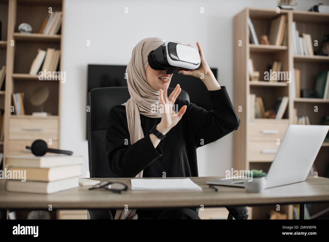 Muslim woman in headset touching virtual screen while sitting at desk ...