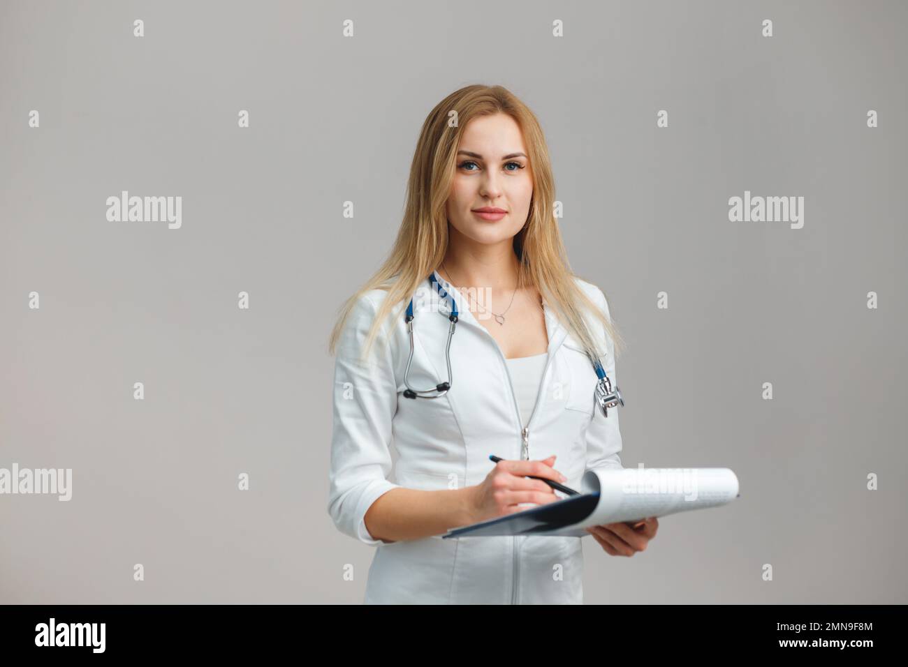 Young European Female Doctor Portrait with stethoscope and folder wearing white robe. Portrait on plain background. Appointment Stock Photo