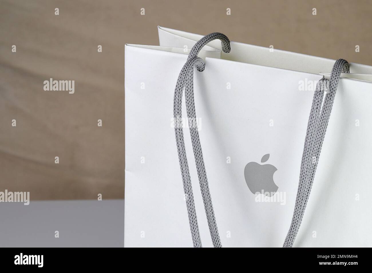 White paper shopping bag, present bag with Apple brand logo standing on white table with shallow focus. Stock Photo