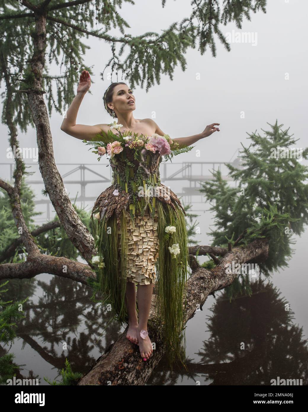 Blooming gorgeous lady in dress of flowers on tree over water in the morning fog Stock Photo