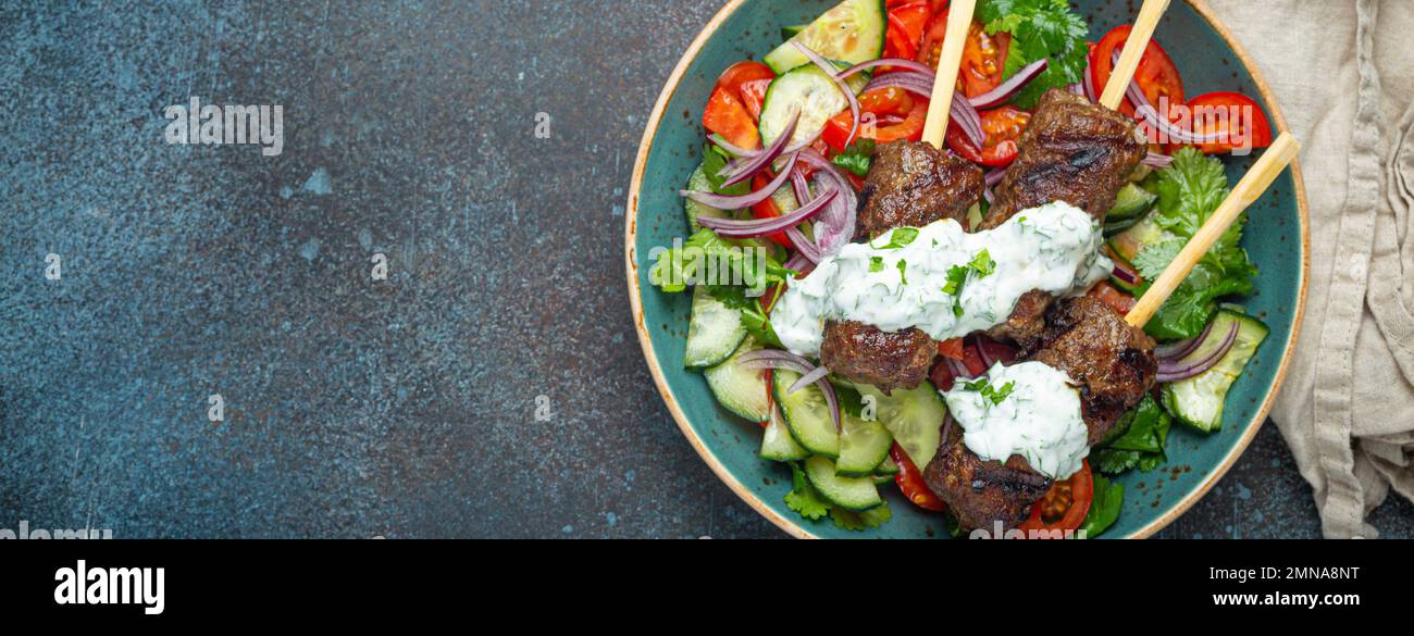 Grilled skewer meat beef kebabs on sticks served with fresh vegetables salad on plate on rustic concrete background from above. Traditional Middle Stock Photo