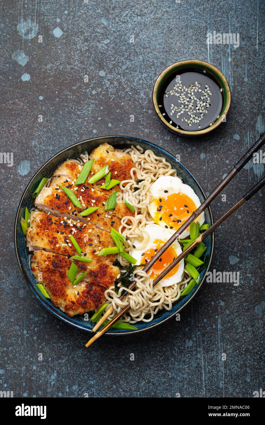 Asian noodles ramen soup with deep fried panko chicken fillet and boiled eggs in ceramic bowl