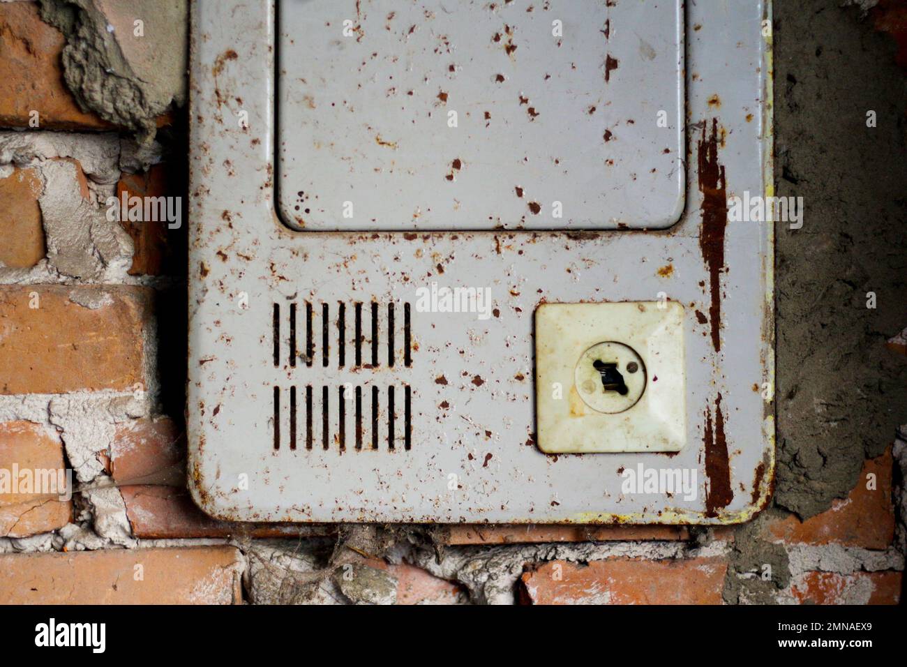 Broken and Damaged Burnt 2 Pin Wall Socket. Blackout concept. Ukraine war. Iron electricity shield on orange old brick wall. Out of focus. Stock Photo