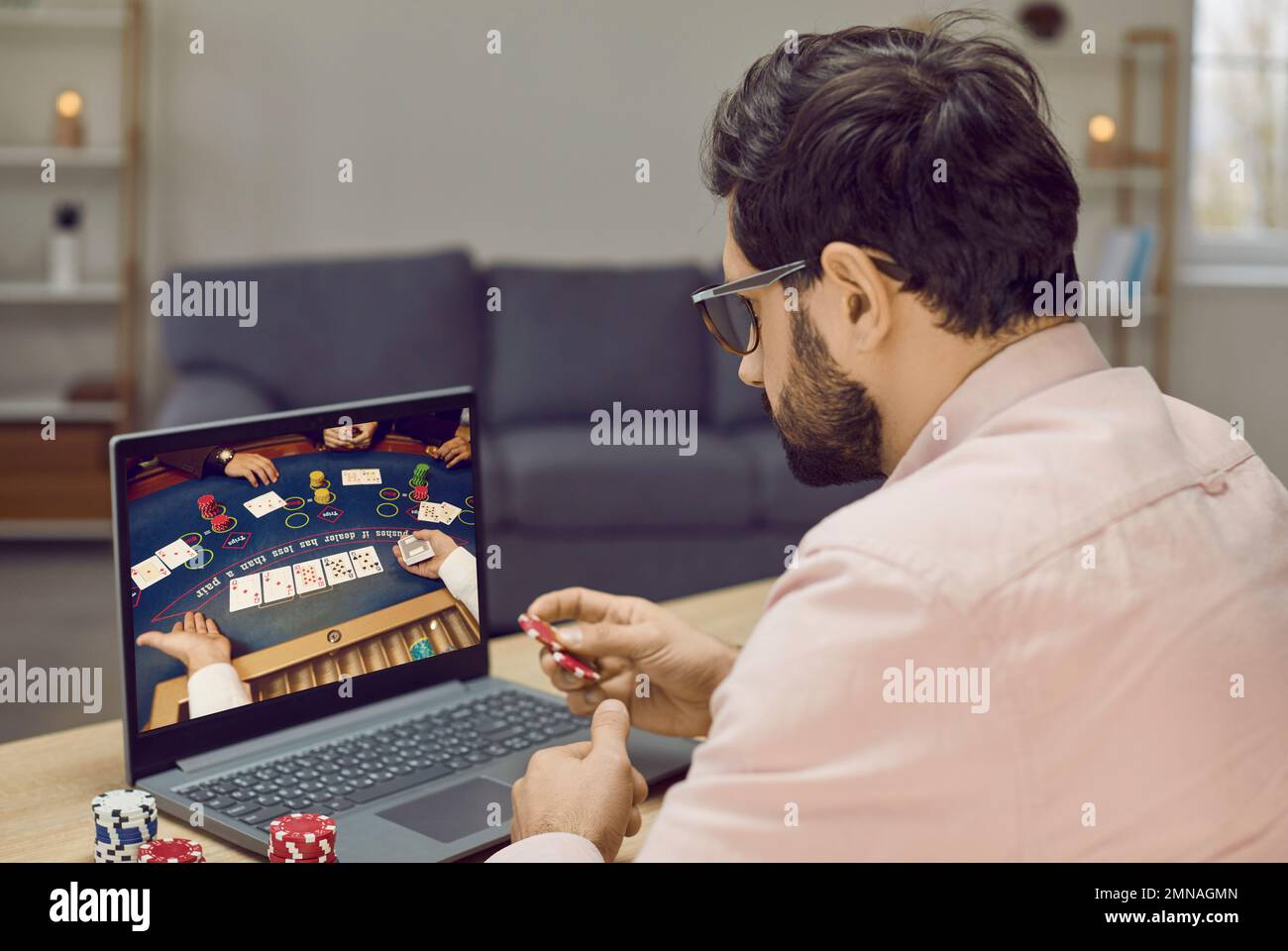 Young gambling man takes part in online poker tournament while relaxing at home. Stock Photo