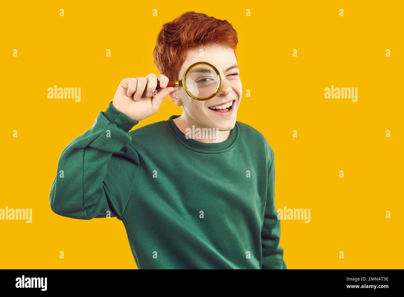 Portrait of cheerful active preteen boy who looks at camera through magnifying glass. Stock Photo
