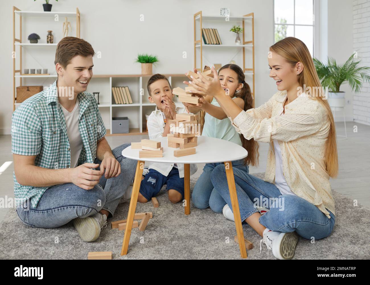 Friendly family with two children are playing tumbling tower sitting on floor at home. Stock Photo
