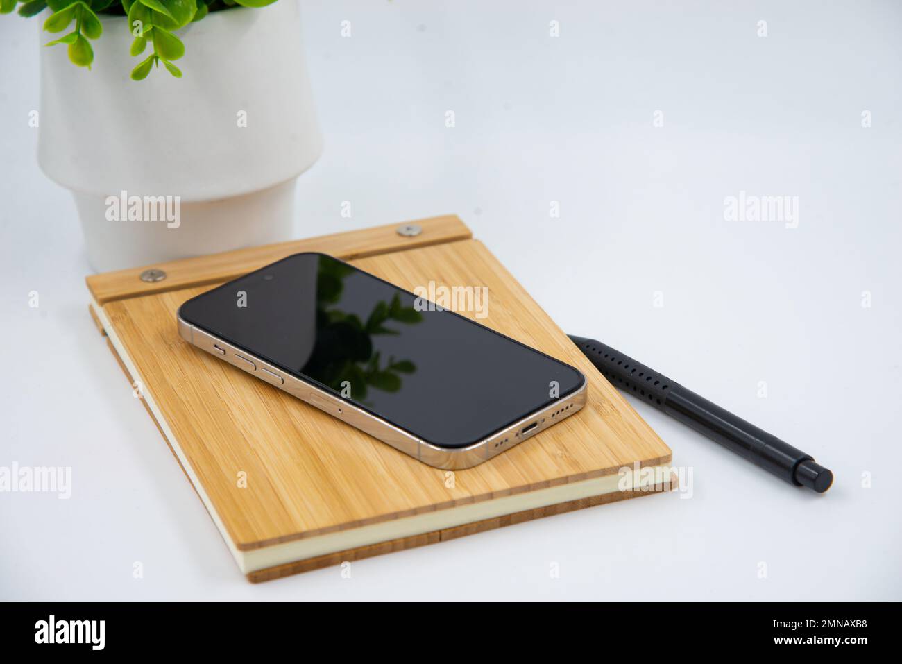 Mobile smart phone with blank screen of gadget on notebook. Digital cell phone with copy space area on white background with pencil and leaf Stock Photo