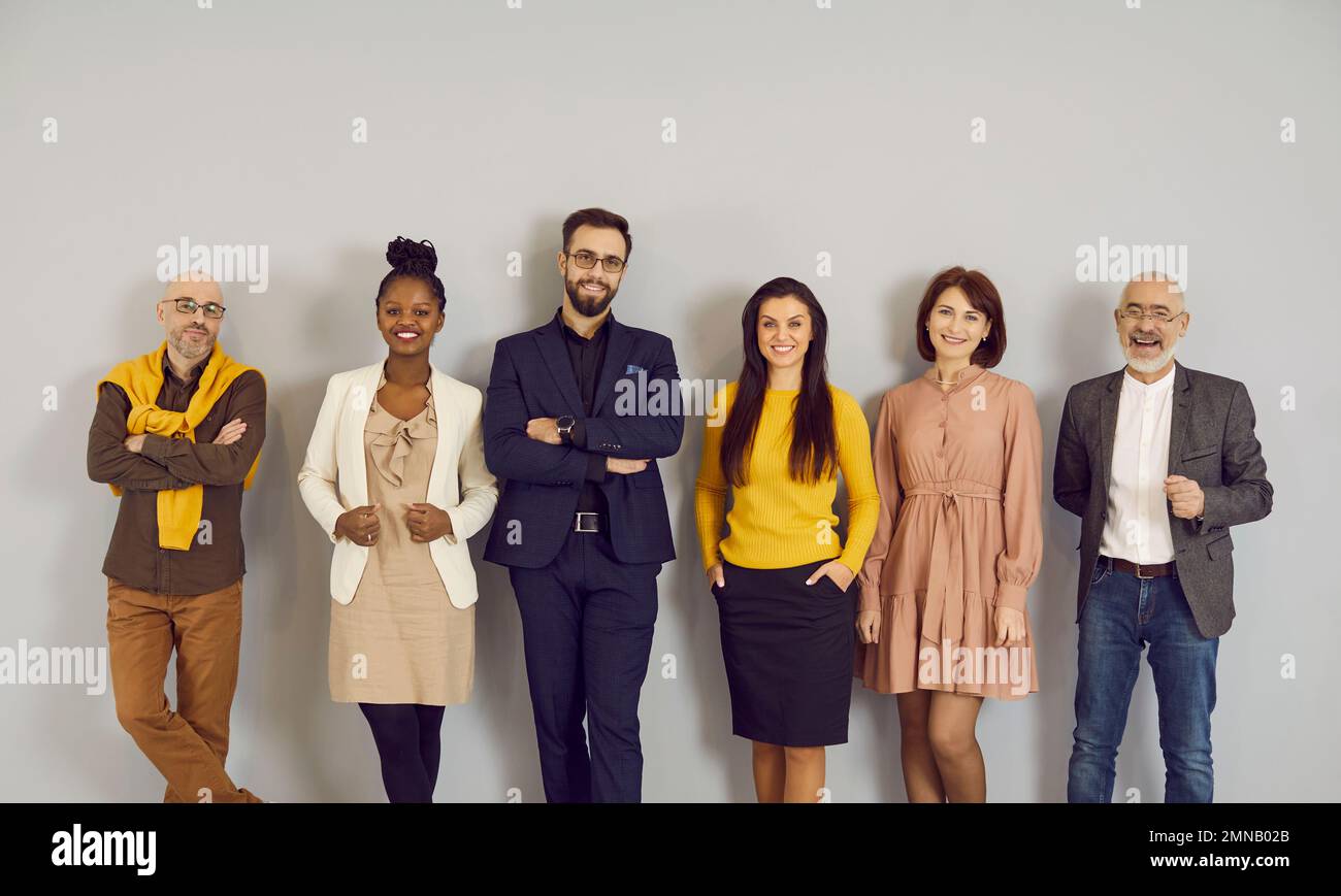 Portrait of multiracial representatives of modern business team standing in row near wall. Stock Photo