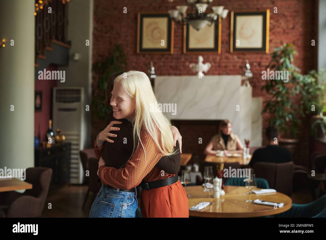 Happy albino girl giving hug to her friend while meeting her in cafe and expressing gladness because of their appointment at leisure Stock Photo