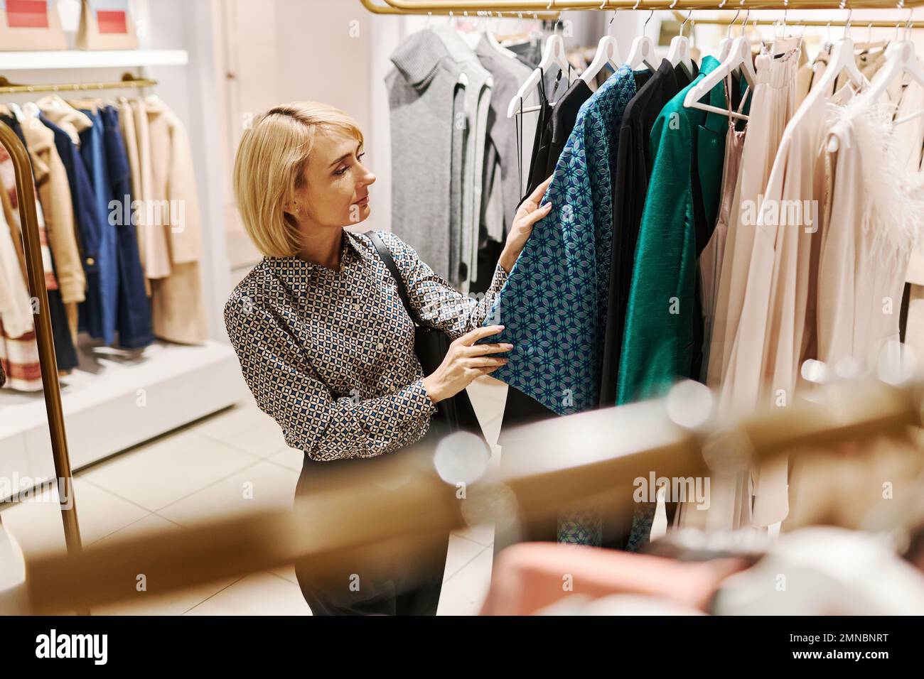 Side view portrait of elegant young woman choosing clothes in luxury boutique, copy space Stock Photo