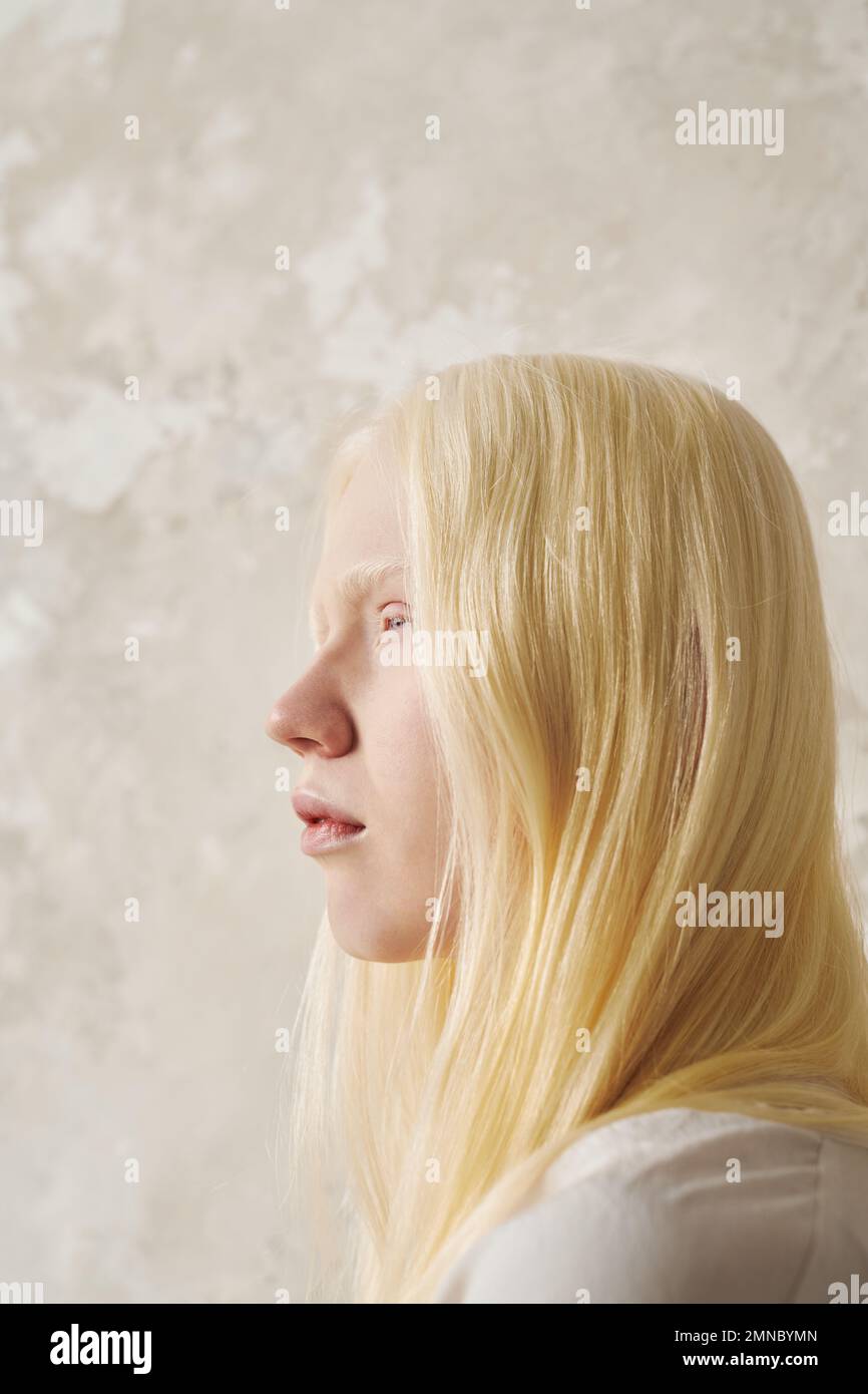 Young serene albino woman with smooth long hair looking forwards while standing in front of camera over wall of pastel color in isolation Stock Photo